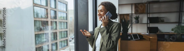 Fototapeta a woman is standing in front of a window talking on a cell phone