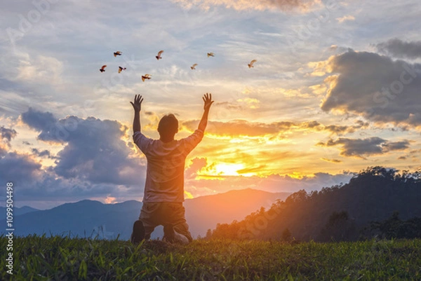 Fototapeta Young male kneeling down with hands open palm up praying to God on the mountain sunset background.
