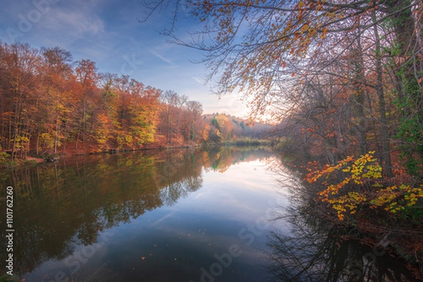 Obraz Autumn colorful foliage over lake with beautiful woods in red and yellow color. Bakony Forest and Mountain, Pisztrangos Lake, Hungary. Long exposure shot.