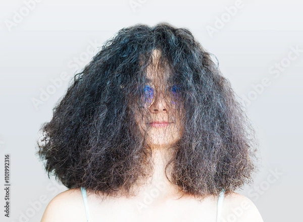 Fototapeta Portrait of a beautiful brunette wearing glasses with lush hair. Girl with tousled hair after blow drying smiling looking at camera.
