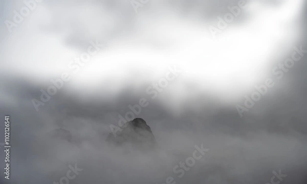 Fototapeta A rocky mountain peak jutting out of the mist and clouds with transparent areas
