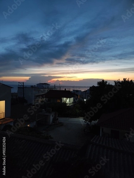 Fototapeta Breathtaking sunset above a coastal city, vibrant hues of orange and pink blending with the serene blue sea. The skyline reflects the golden hour glow, creating a dreamy, tranquil atmosphere.