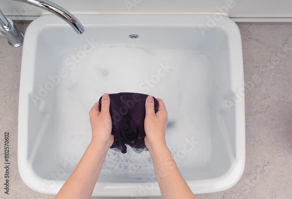 Fototapeta Handwashing violet clothes in a sink filled with soapy water, highlighting a simple and effective laundry routine.