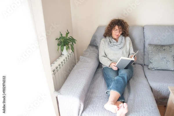 Fototapeta Relaxed Lady Reading A Book In A Cozy Room With Natural Decor, Promoting Ideas Of Self-Improvement, Learning, Relaxation, Indoor Lifestyle, And Enjoying Peaceful Moments At Home