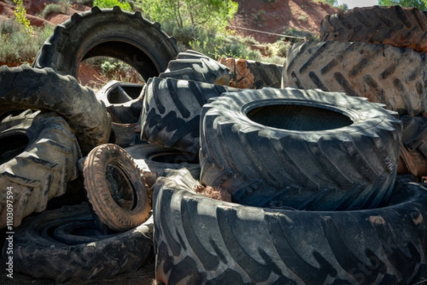 Fototapeta A pile of large worn tractor tires stacked in the field