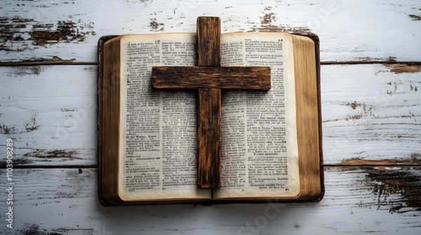Obraz A wooden cross resting on an open Bible, symbolizing faith and the profound meaning of its words. The scene is set against a clean, white wood-paneled background, creating a serene and spiritual atmos