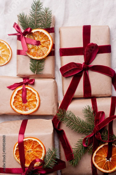 Fototapeta Wrapped gifts with dried orange and velvet pine branches and bows on white linen Christmas decoration diy recipe copy space flat lay top view holiday inspiration
