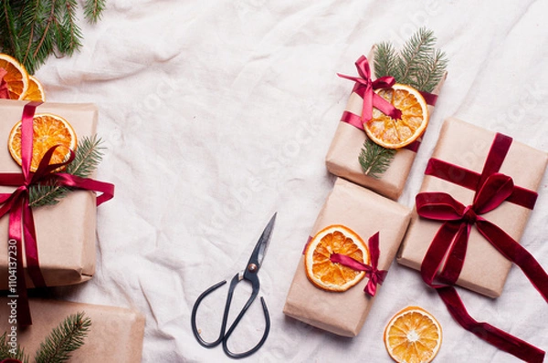 Fototapeta Wrapped gifts with dried orange and velvet pine branches and bows on white linen Christmas decoration diy recipe copy space flat lay top view holiday inspiration