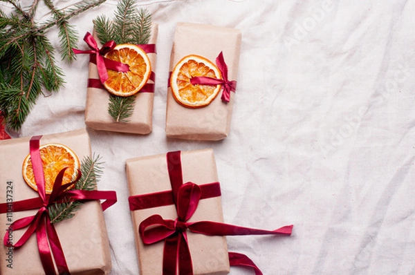 Fototapeta Wrapped gifts with dried orange and velvet pine branches and bows on white linen Christmas decoration diy recipe copy space flat lay top view holiday inspiration