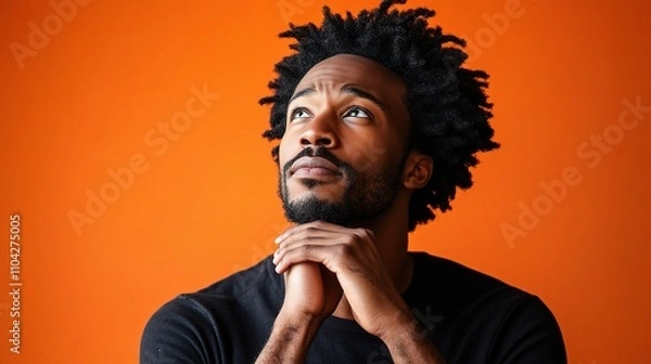 Fototapeta Thoughtful man with textured hair gazing at vibrant orange background