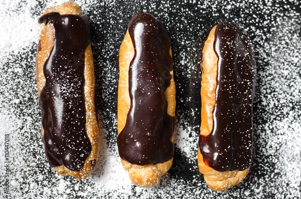 Fototapeta Eclairs with chocolate on a black background with powder
