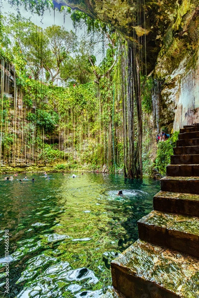 Fototapeta Ik Kil Cenote, Mexico - January 2, 2022 Chichen Itza, Enchanting cenote featuring crystal-clear water, hanging vines, and lush greenery, with a stone staircase leading to the natural pool High-quality