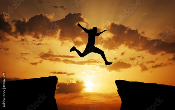 Fototapeta Man jumping across the gap from one rock to cling to the other.