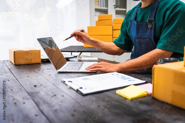 Fototapeta Close-up of a businessman’s hand packing items at a desk, preparing products for shipping. Highlighting delivery services for private companies online shopping with credit cards for convenience