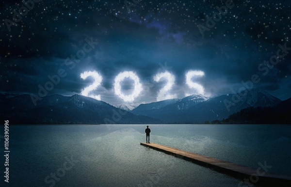 Fototapeta New year 2025 at night, man standing on a wooden jetty on a lake and looking to the cloudy numbers in the dark sky with stars over mountains, copy space