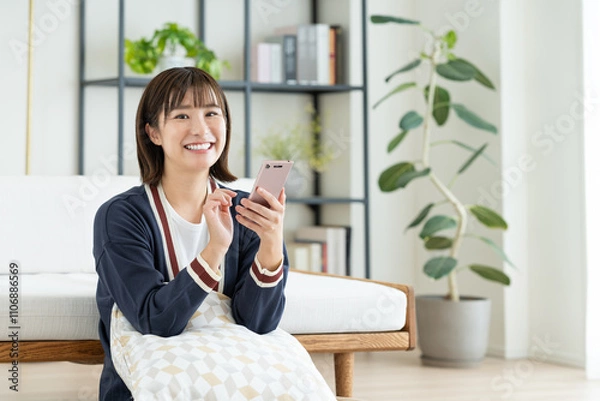 Fototapeta リビングでスマホを見る若い女性