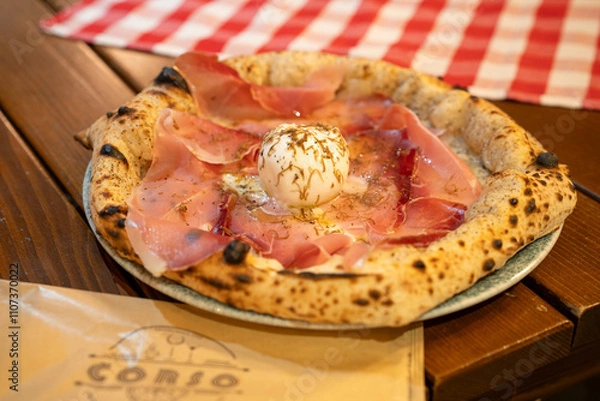 Fototapeta A close-up view of a pizza topped with burrata and thinly sliced prosciutto showcases its freshness and appeal.