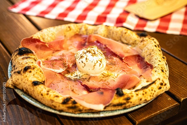Fototapeta A delicious pizza topped with fresh prosciutto and creamy burrata, presented on a rustic plate.