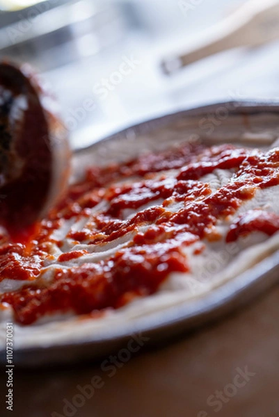 Fototapeta Fresh tomato sauce is evenly spread on a pizza base, capturing the start of a flavorful journey.