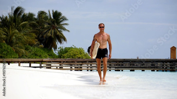 Obraz Young guy with a surfboard on the beach