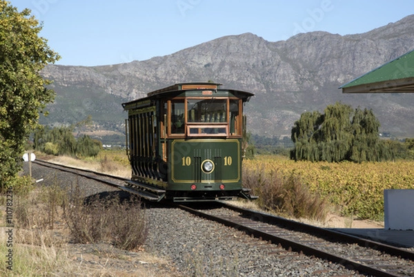 Obraz FRANSCHHOEK ZACHODNI PRZYLĄDEK AFRYKA POŁUDNIOWA. Pociąg turystyczny przy winnicy Rickety Bridge w dolinie Franschhoek. Pasażerowie przejeżdżają przez malownicze winnice tego regionu w Western Cape