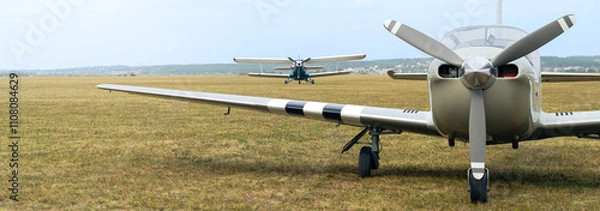 Fototapeta Biplane and small sport airplane with propeller, panoramic landscape with two aircraft on airfield.
