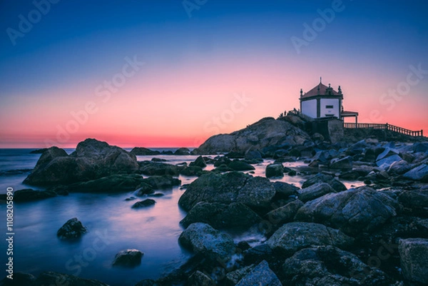 Obraz The senhor da pedra chapel stands on a rocky outcrop along the coast of vila nova de gaia, portugal, bathed in the warm glow of the setting sun, creating a serene and picturesque scene