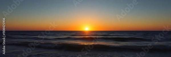 Fototapeta The setting sun casts a golden glow over the ocean as the day succumbs to night, light, waves, clouds