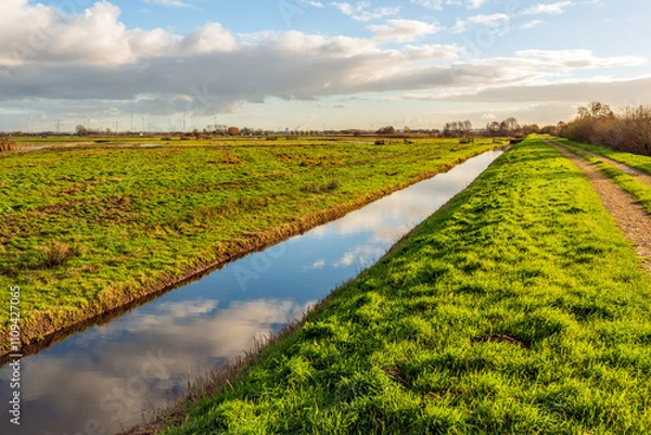 Fototapeta Dutch polder landscape with a straight ditch. It is a windless day in the autumn season and the clouds are reflected in the mirror-smooth water surface.