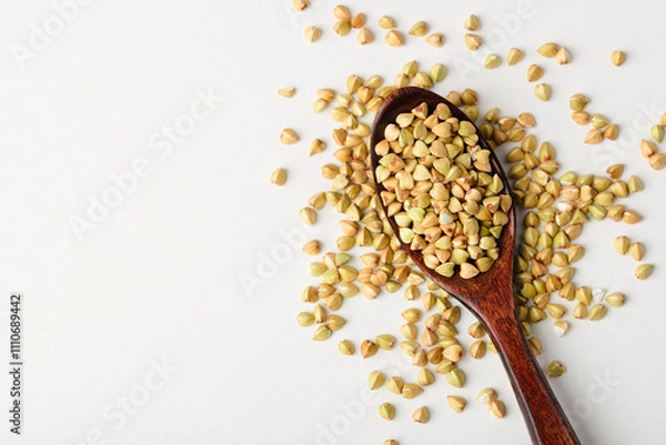 Fototapeta Dietary green buckwheat groats in a wooden spoon close-up isolated on white background copy space