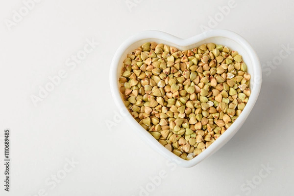 Fototapeta Dietary green buckwheat groats in a heart-shaped bowl isolated on white background, top view with copy space