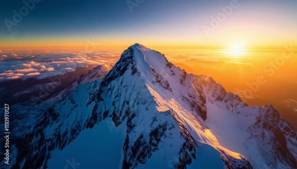 Fototapeta An aerial view of a majestic snow-covered mountain peak at sunrise. The mountain’s jagged edges are