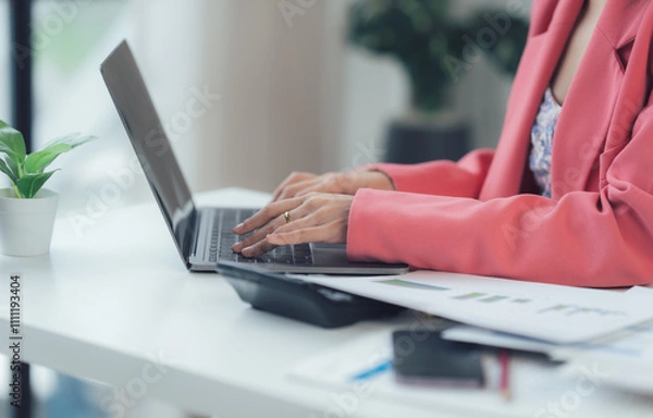 Fototapeta Focused and Determined: A businesswoman in a pink blazer works intently on her laptop, surrounded by paperwork and a calculator, showcasing the dedication and focus required for success. 
