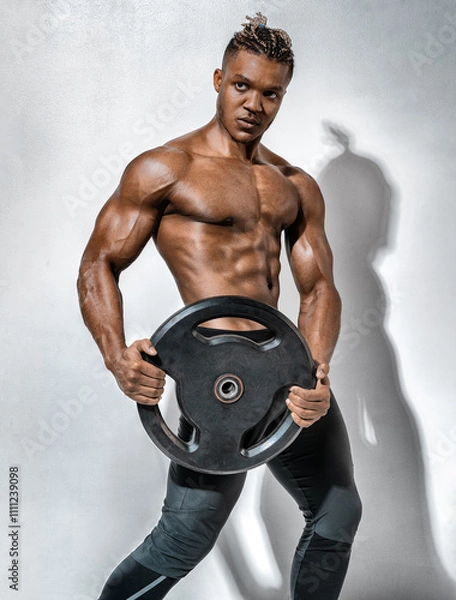 Obraz Athletic man doing exercise with heavy weights plate. Photo of man with naked torso on gray background. Strength and motivation