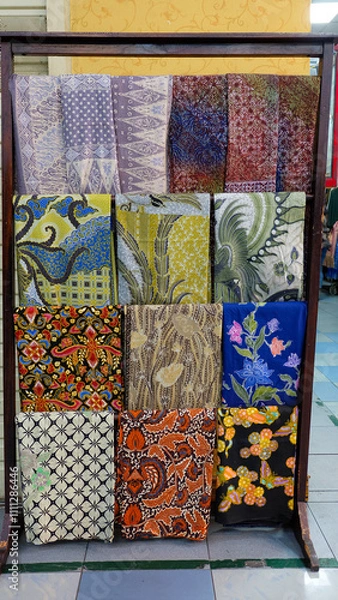 Fototapeta Colorful batik fabrics displayed on a wooden rack. Close-up shot highlights intricate patterns and vibrant colors. Perfect for fashion blogs or promoting Indonesian culture