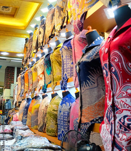 Fototapeta Colorful batik shirts displayed on mannequins in a shop. Selective focus on the shirts, wide-angle shot captures the vibrant display. Perfect for fashion blogs or promoting Indonesian culture