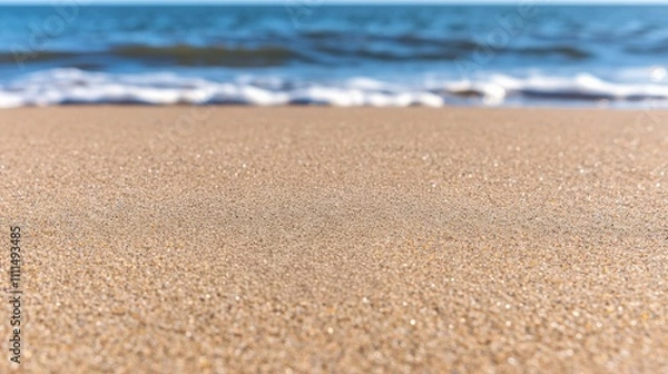 Fototapeta Sandy beach foreground with gentle waves and a clear blue ocean background, creating a serene coastal atmosphere.