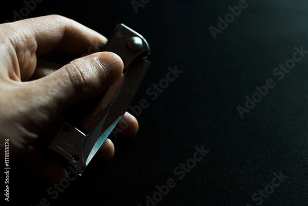 Obraz Folding knife in hand with wooden handle on dark background