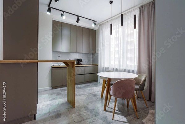Fototapeta Modern kitchen in a small cozy contemporary studio apartment. Table and chairs in the foreground. Built in household appliance