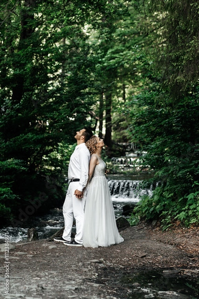 Fototapeta A large waterfall with very cold water and slippery stones, its height is more than 8 meters, the bride and groom are standing on the stones, this photo was taken with a long exposure