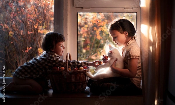 Obraz Brother and sister are playing with their white cat and a basket of apples