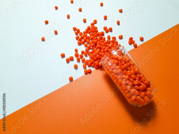 Fototapeta Orange masterbatch granules with glass tube on white and orange background,color pigment carrier polymer in plastic industry.Suitable for plastic company catalog design