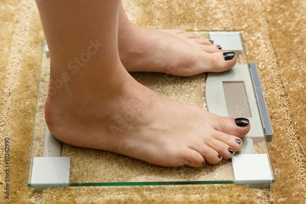 Obraz Close up female feet on digital weighti scale