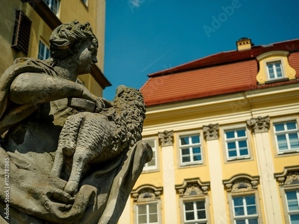 Fototapeta Detailed stone statue of a figure holding a sheep in front of a historic building in Poland