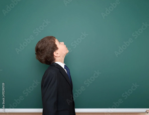 Fototapeta school boy in black suit look up on green chalkboard background, education concept