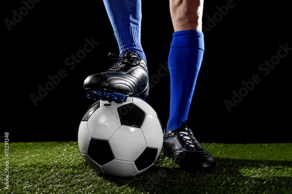 Obraz legs and feet of football player in blue socks and black shoes posing with the ball playing on green grass