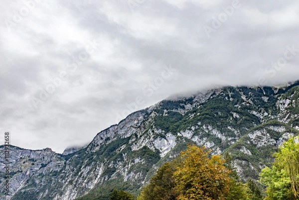 Fototapeta A mountain range covered in mist with forested slopes and rocky textures, surrounded by lush greenery