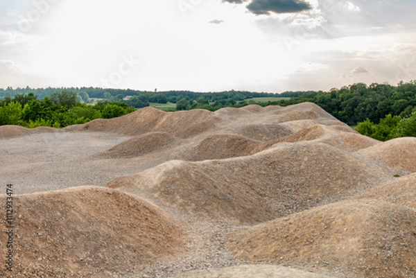 Fototapeta Rolling sand hills near a quarry, blending earthy tones with lush green fields and a serene afternoon sky