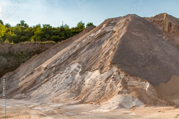 Fototapeta A towering sand pile near a quarry, highlighted by natural sunlight and lush greenery in the backdrop