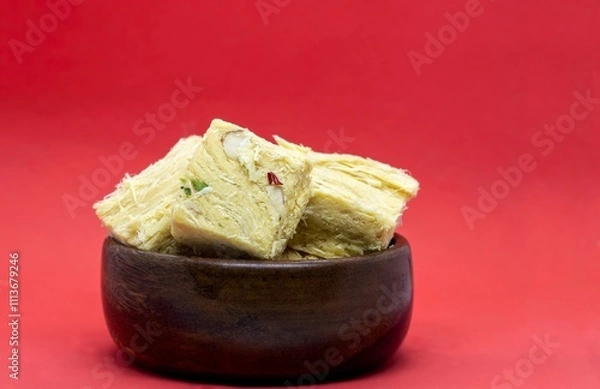 Obraz Soan Papdi or Patisa Garnished with Cashew Nut, Pistachio, Almond and Saffron in Wooden Bowl Isolate on Red Background with Copy Space, Also Known as Shompapri or Shonpapdi